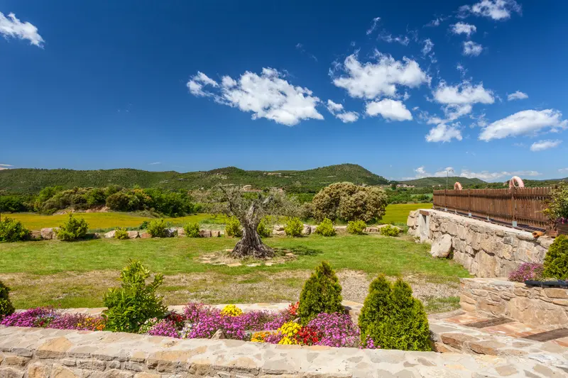 Jardí exterior amb flors i murs de pedra de la masia