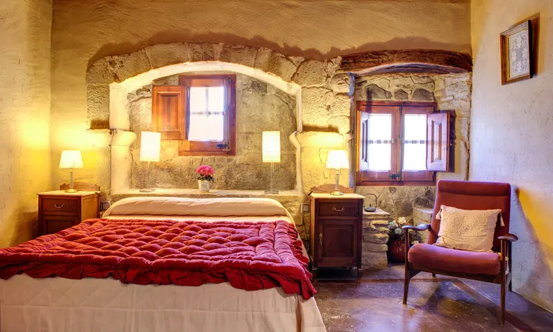 Habitació doble amb parets de pedra i cobrellit vermell